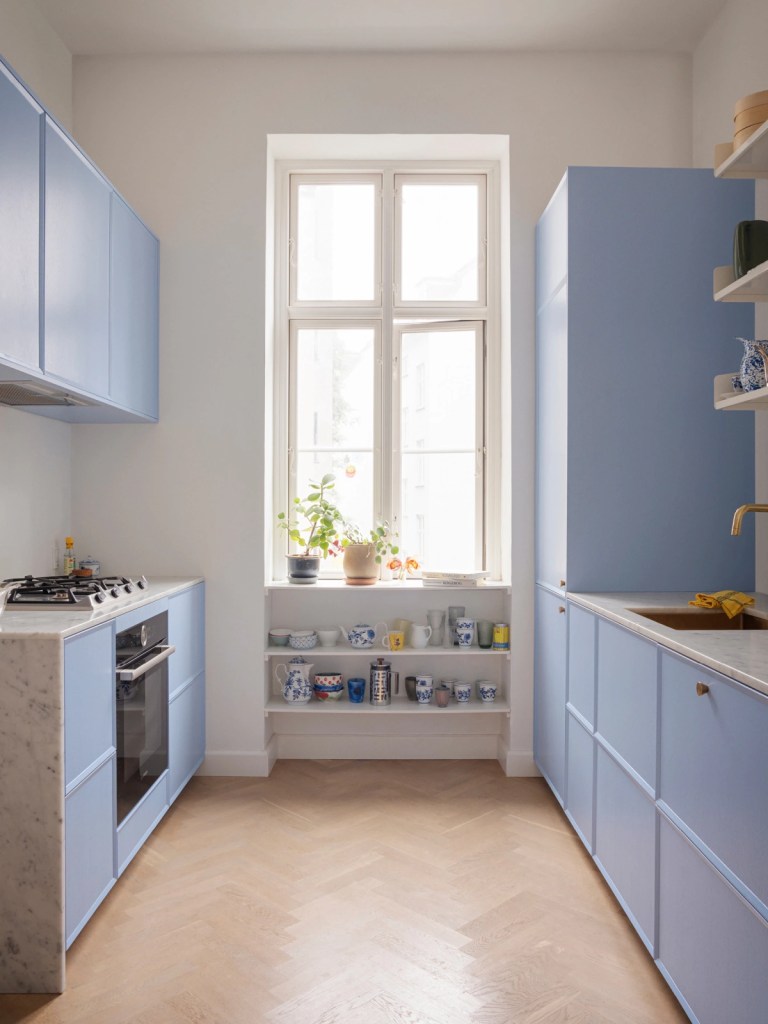 A light blue galley kitchen with brass hardware and white marble countertops