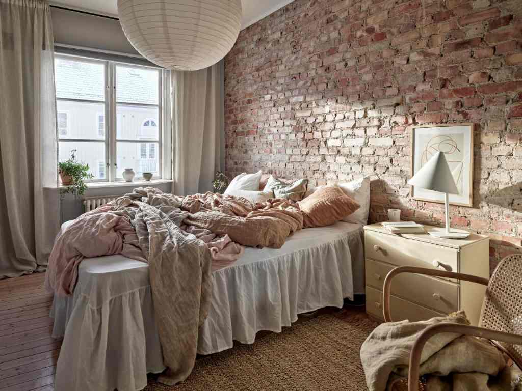 A bedroom with an exposed brick wall and a mixture of linen throw pillows in warm colors