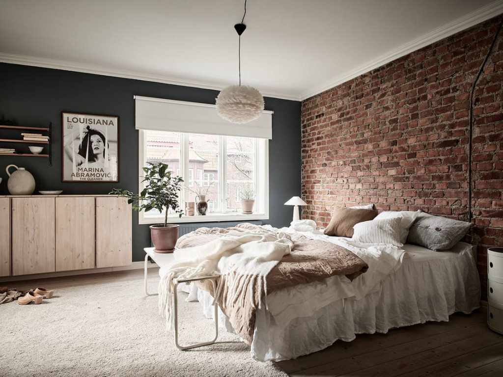 A bedroom with a dark blue wall color and an exposed brick wall above the bed