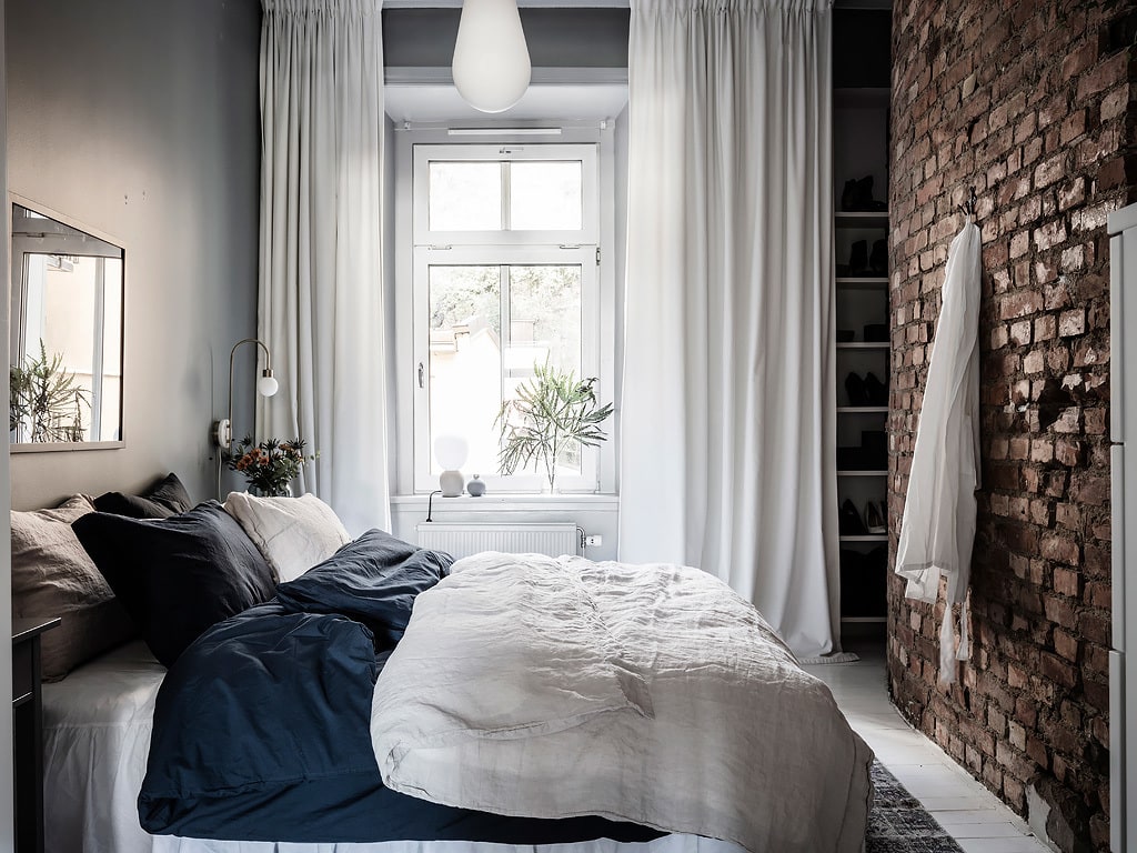 A grey bedroom with a section of the brick exposed