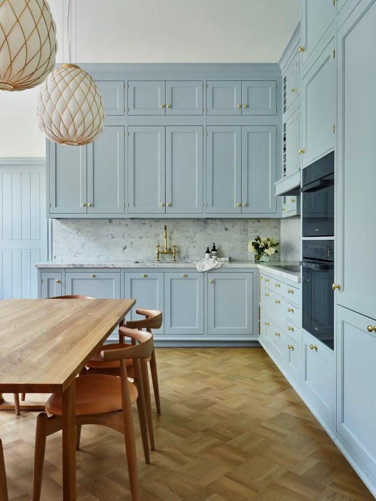 A floor to ceiling light blue kitchen with gold hardware and white marble countertops