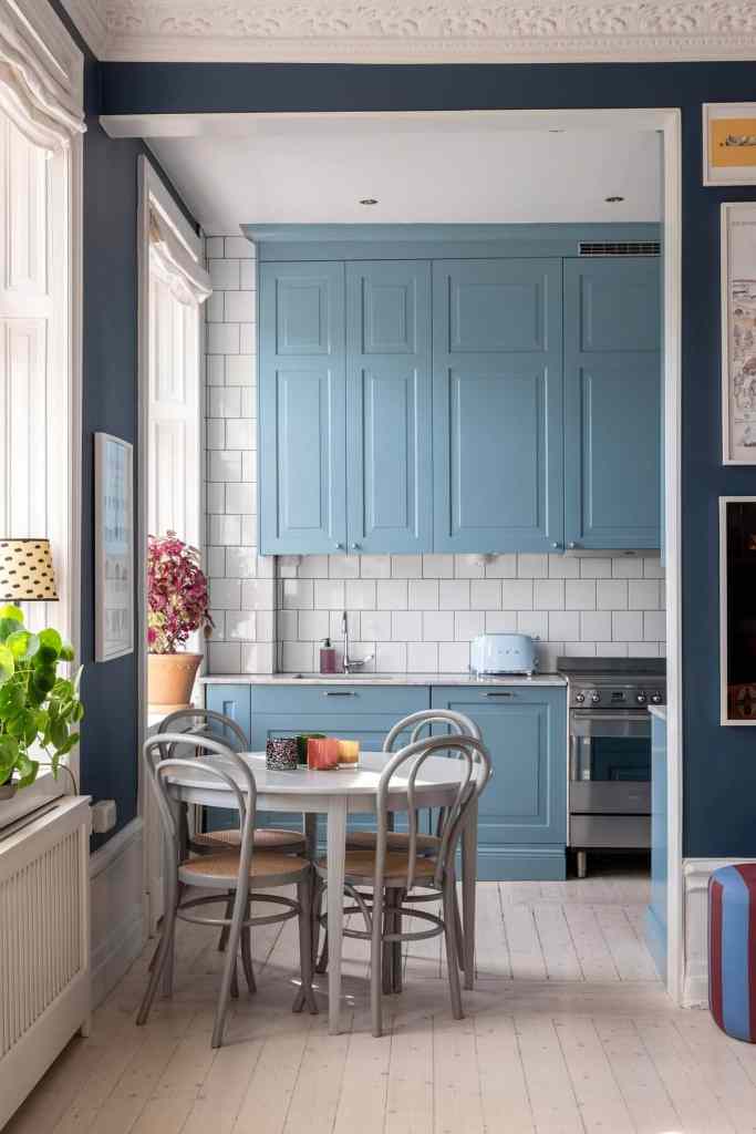 A light blue farmhouse kitchen with a light grey dining table and chairs