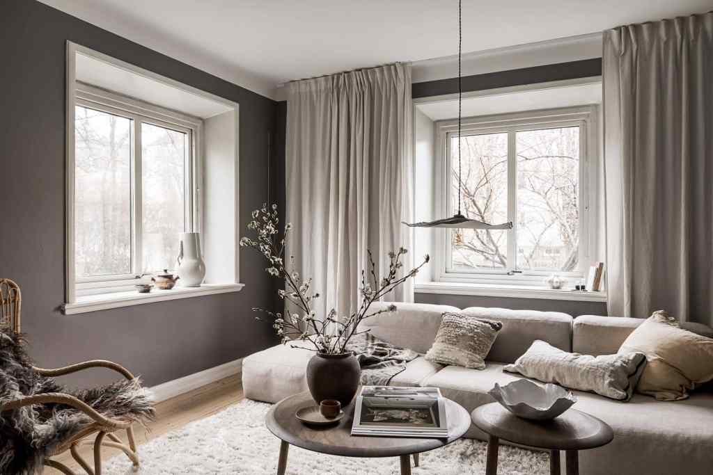 A living room with dark grey walls, a beige fabric sofa and dark oak coffee tables