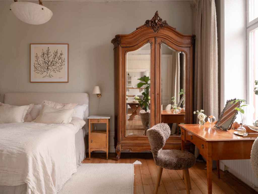 A bedroom with a white color palette and warm wood tones coming from antique furniture pieces