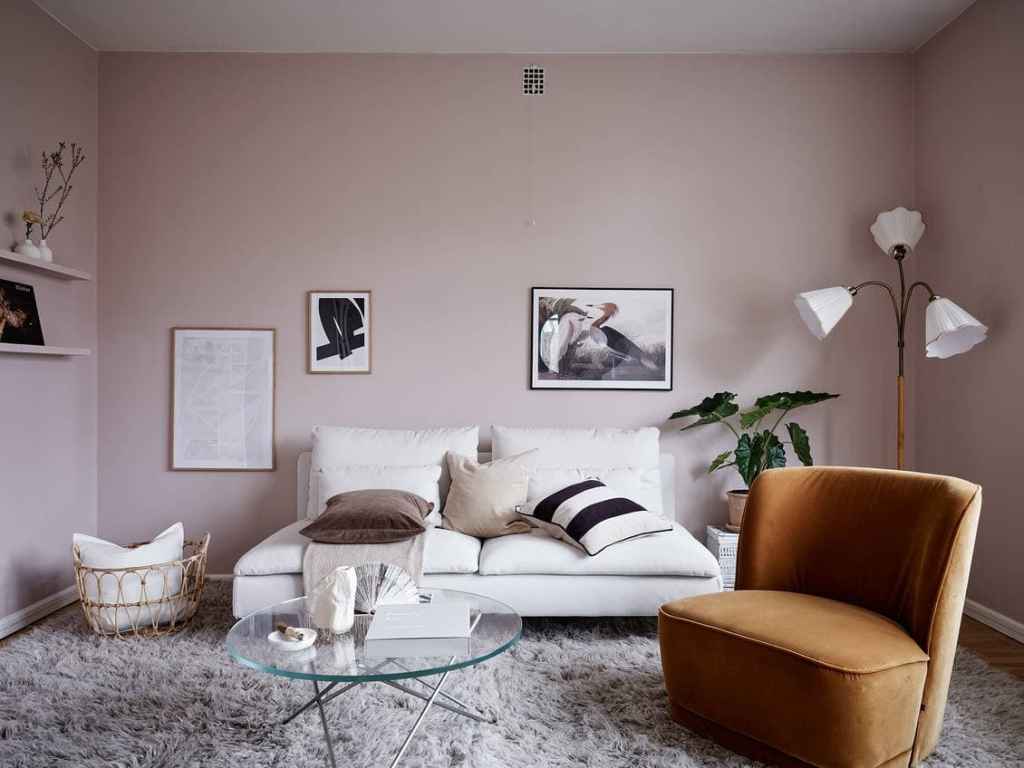A living room with pink walls, a white couch and a velvet club chair