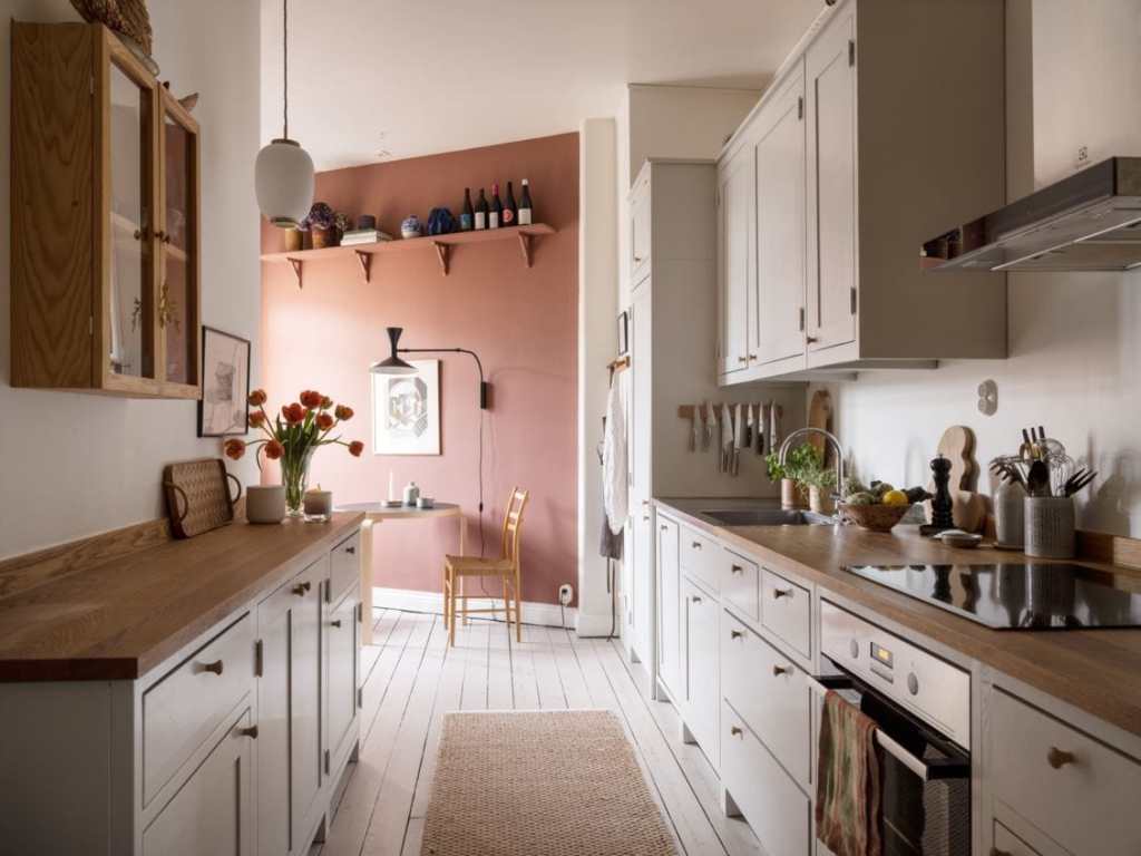 A white galley kitchen comes out in a dining area with a terracotta wall