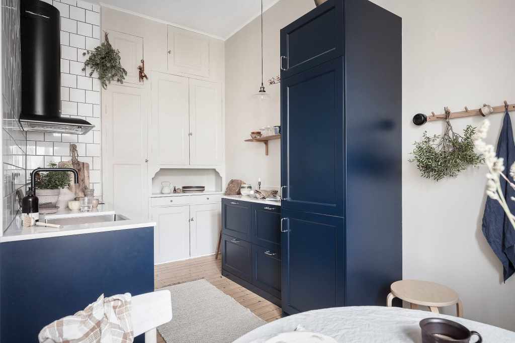 A navy galley kitchen with a white pantry