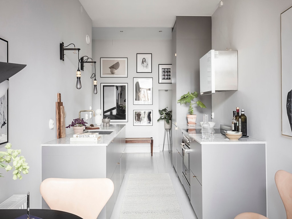 A grey galley kitchen with white marble countertops and a gallery wall