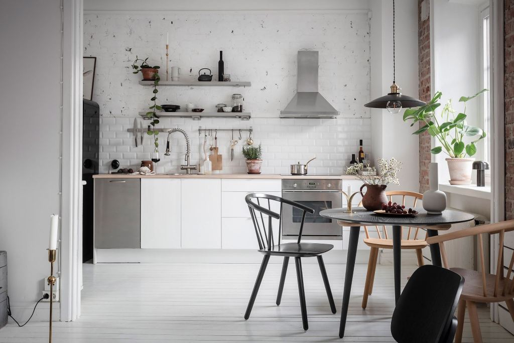 A white kitchen with a tile backsplash and a white-painted exposed brick wal;