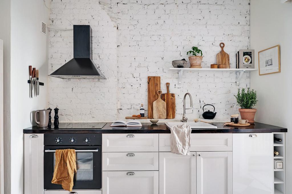 A white kitchen with black countertops and a white-painted brick wall