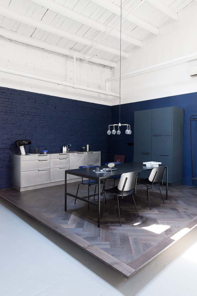 A blue painted brick backsplash in a stainless steel kitchen with a black dining table