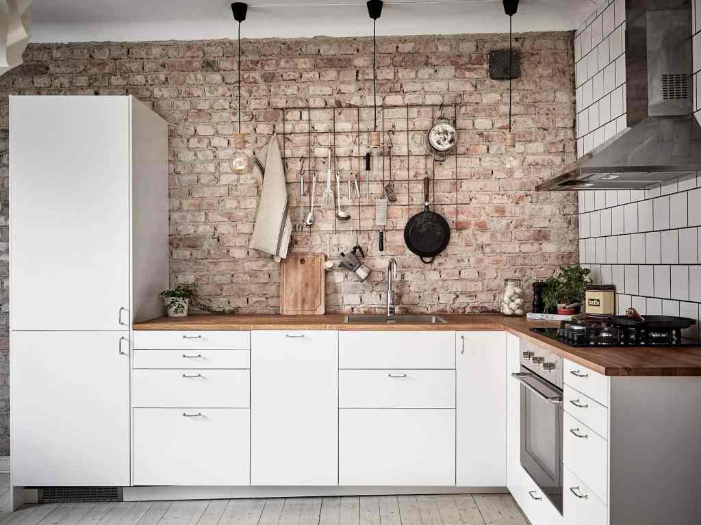 A simple white kitchen with a wood countertop and an exposed red brick backsplash