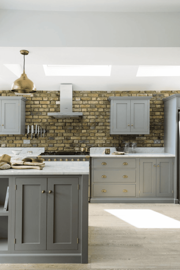 Yellow brick walls in a light grey shaker kitchen with white marble countertops