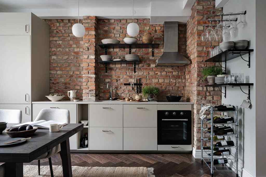 A minimal off-white kitchen with an impressive red brick backsplash and a stainless steel hood