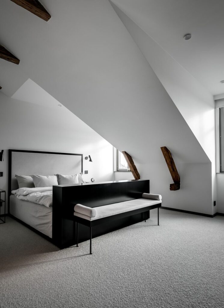 A modern attic bedroom with white walls and a black bed