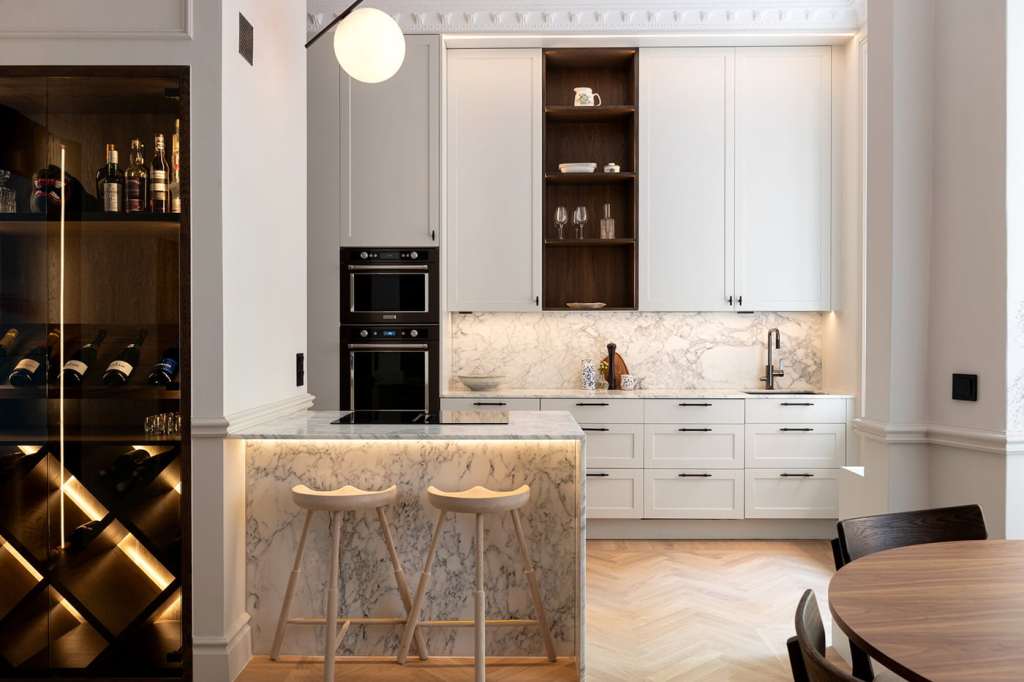 A white shaker kitchen with a white marble kitchen island and dark wood cabinet inlays