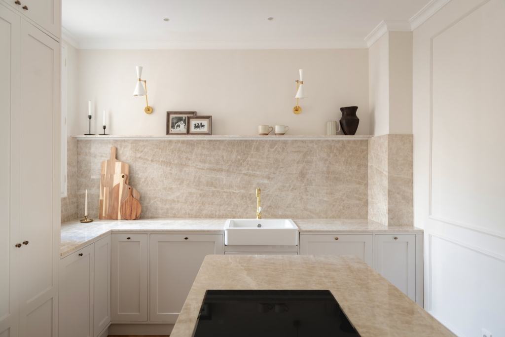A narrow white farmhouse sik in an off-white kitchen with beige stone countertops