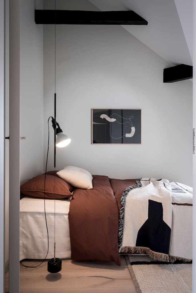 An attic bedroom with white walls and brown textiles on the bed
