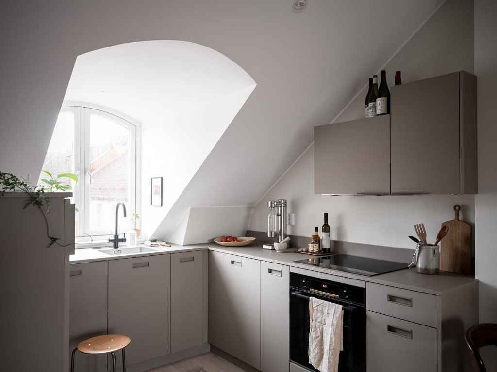 A U-shaped kitchen with light grey cabinets in a small attic studio apartment