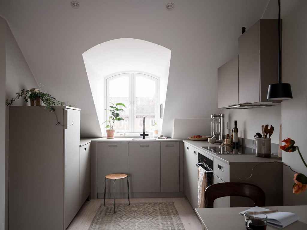 A U-shaped kitchen with light grey cabinets in a small attic studio apartment