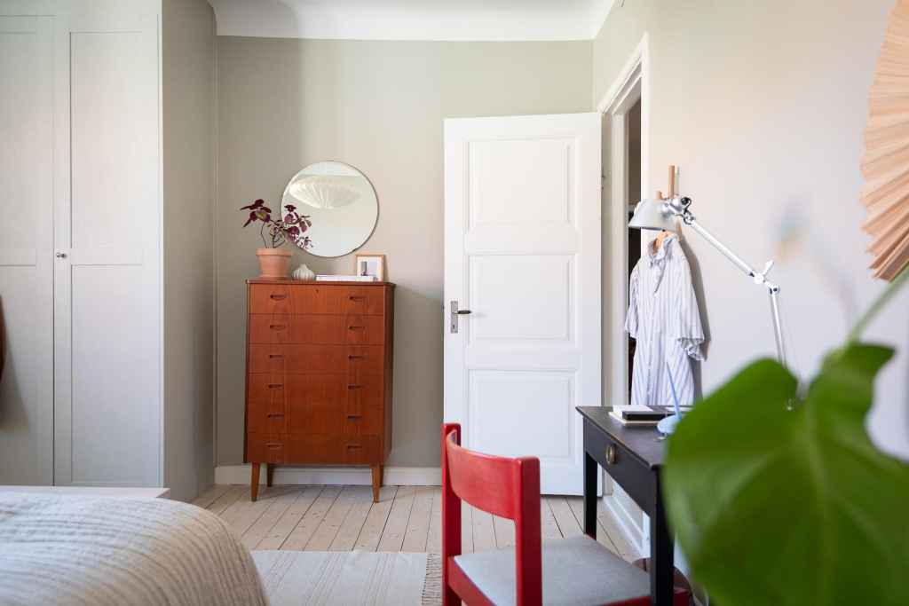 A bedroom with a light grey wall color, wardrobe in the same color and a vintage dresser