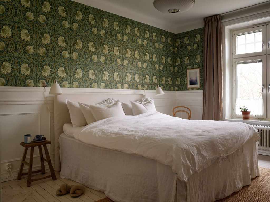 A master bedroom with white wainscoting and green floral wallpaper on the upper half