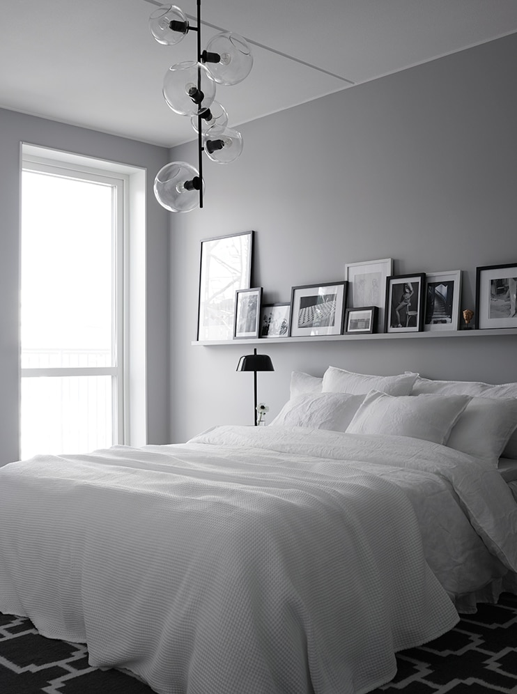 A monochrome bedroom with white bedding and a black and white gallery wall on a picture ledge