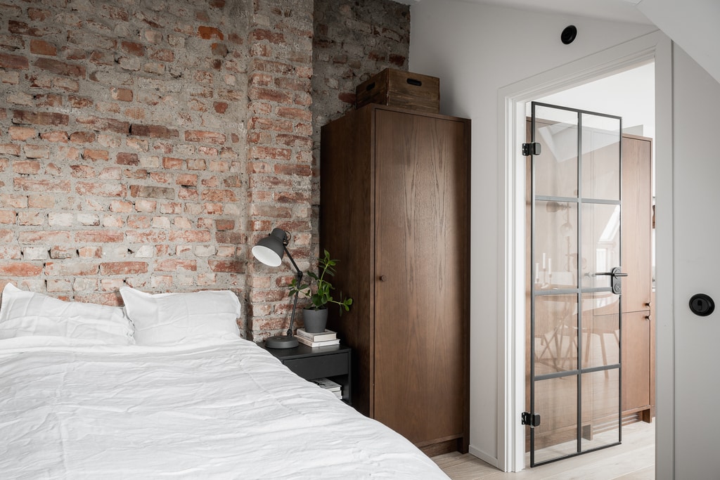 A bedroom with an exposed brick wall and a walnut wardrobe cabinet