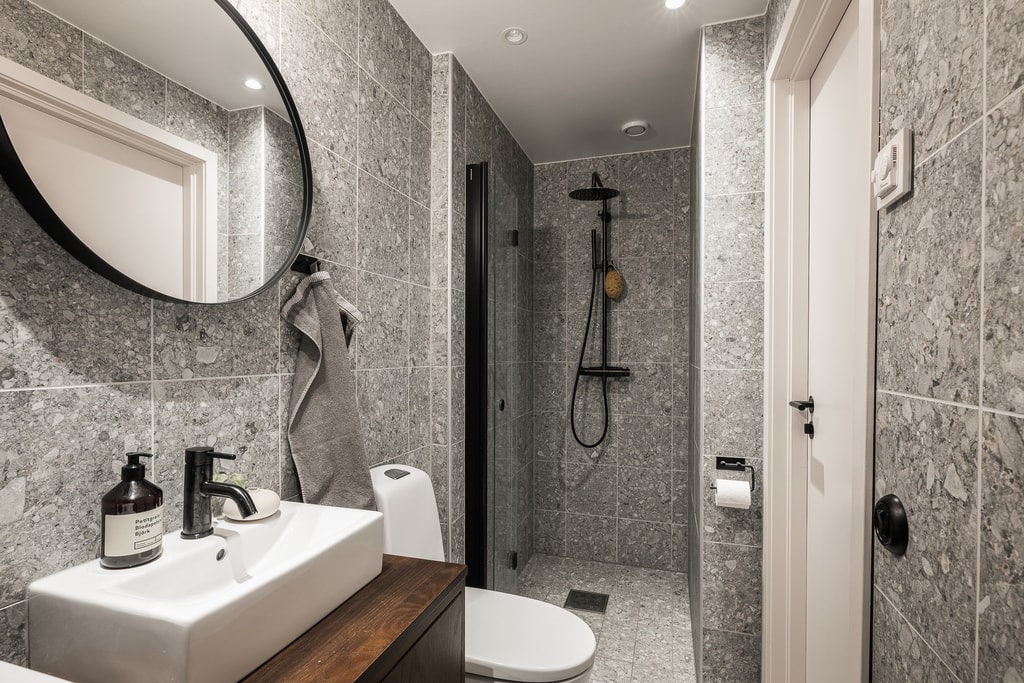 A modern bathroom with grey terrazzo tiles, a walnut vanity and black fixtures