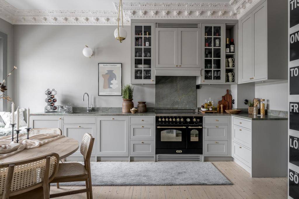 A classy L-shaped kitchen with grey shaker cabinets and marble countertops
