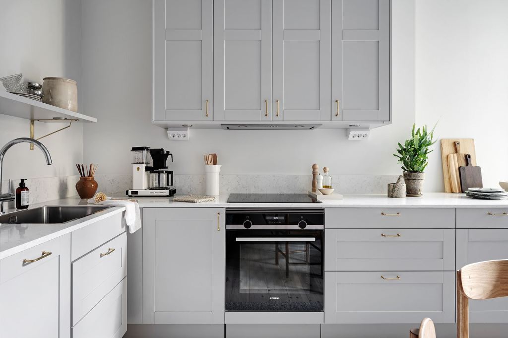 A light grey shaker kitchen with white marble countertops and gold hardware in an L-shaped layout