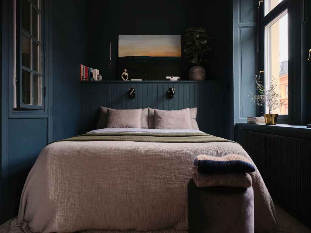 A bedroom with dark blue walls, beige bedding, white ceiling