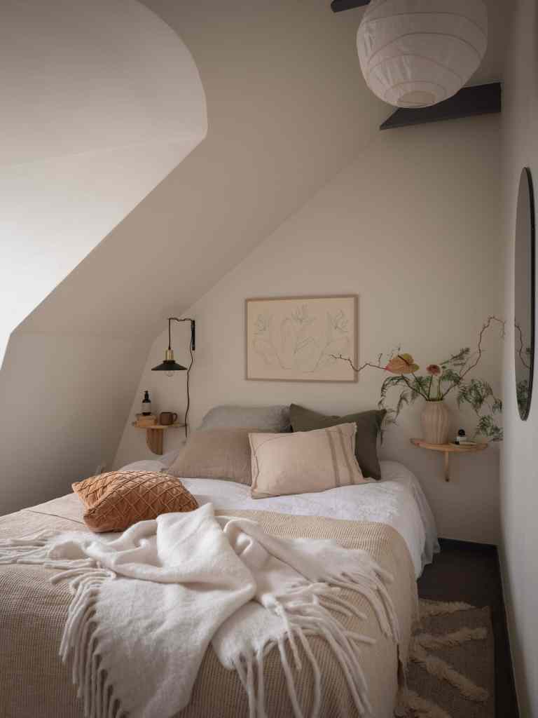 A small bedroom with grey floors underneath a sloped roof