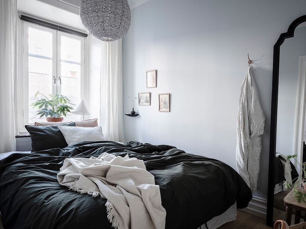 A small bedroom with light blue walls and black bedding